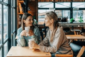 Two moms talking over coffee, smiling and sharing a real “mommy 2 mommy” moment