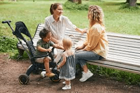 Diverse moms at a park, children playing nearby, as they chat and laugh—a true “mommy 2 mommy” scene
